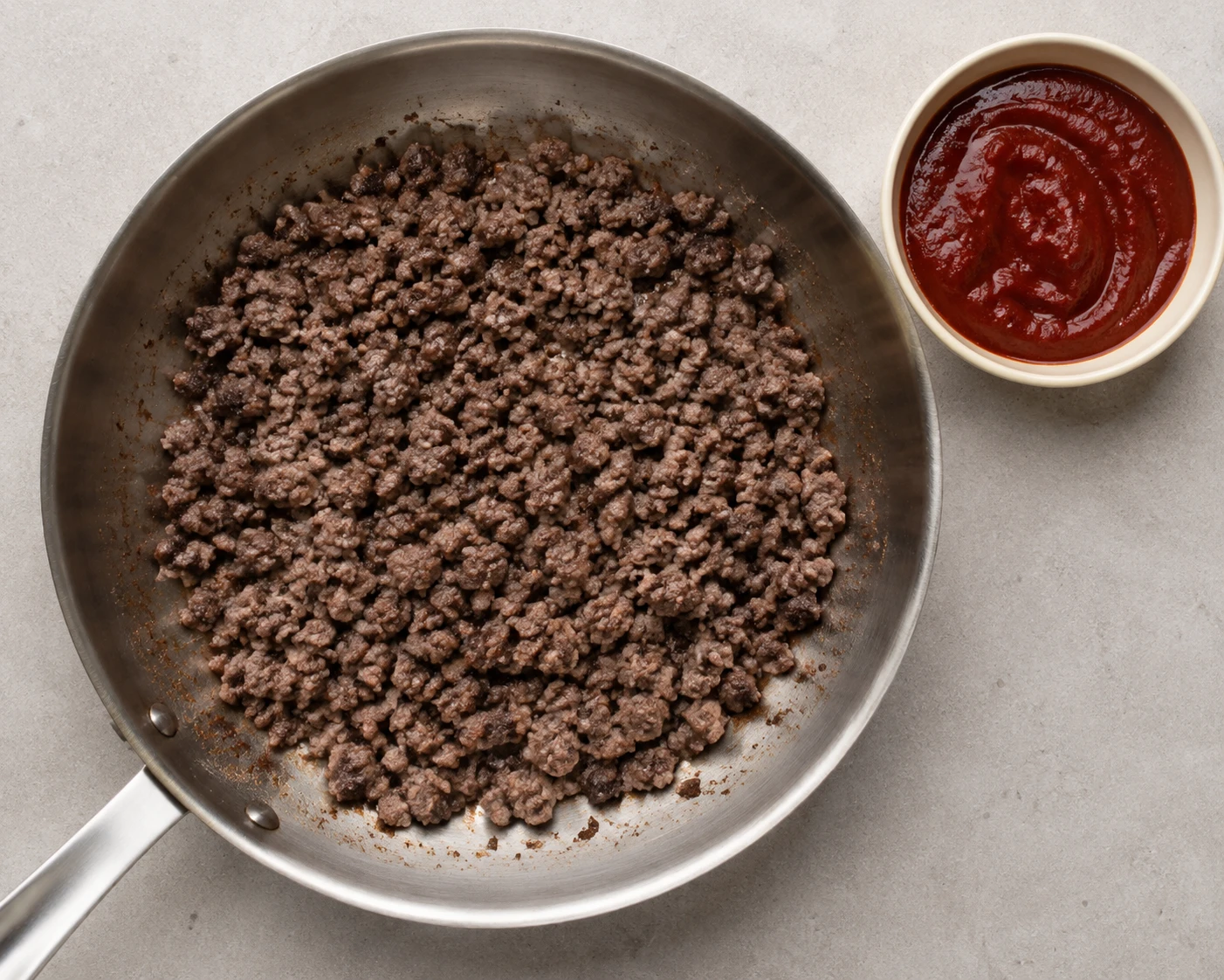 Lean ground beef browns in small crumbles in a wide skillet beside red gochujang sauce.