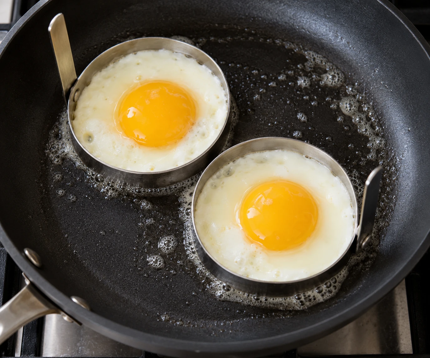 Eggs cook in rings in a lightly buttered skillet until their whites turn opaque.