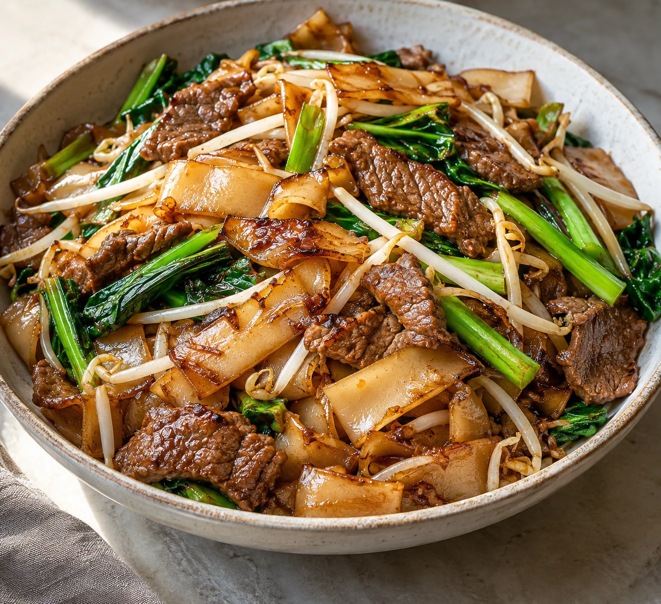 Wide rice noodles with browned edges are tossed with sliced beef, Chinese broccoli, scallions, and bean sprouts.