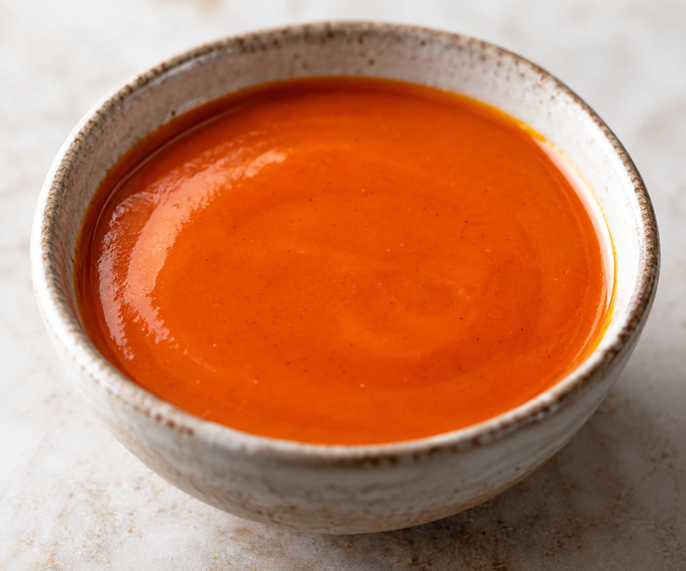 A close view shows the smooth, glossy orange surface of finished Buffalo sauce.