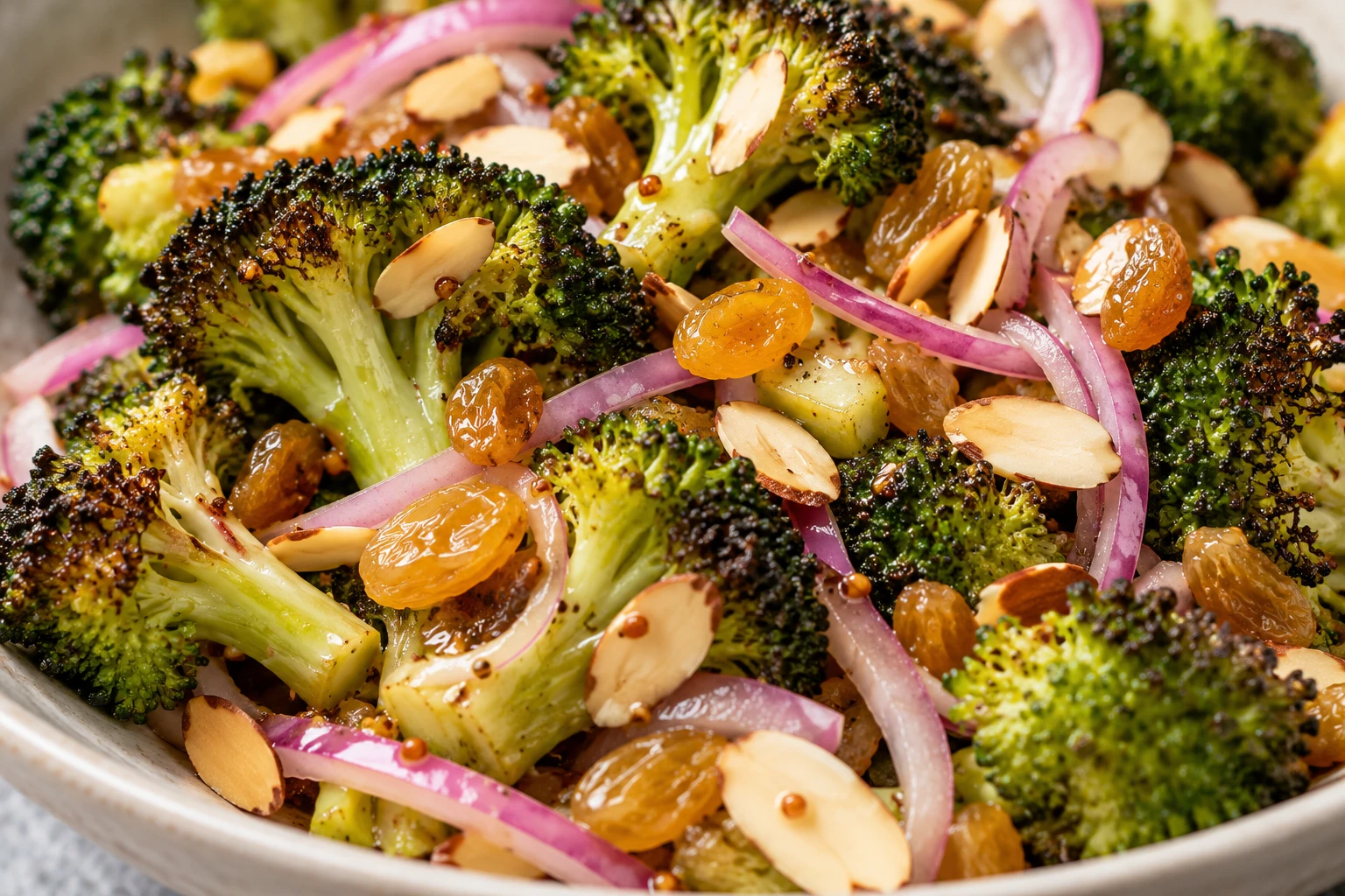 Smoky broccoli crowns carry lemon-Dijon dressing, golden raisins, fine red onion, and crisp almonds.