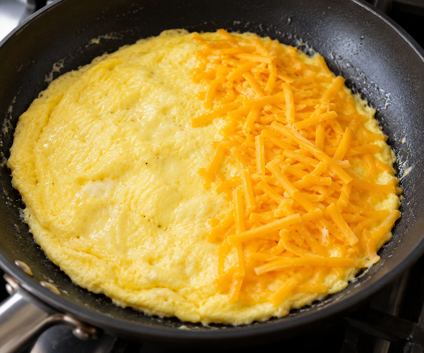 Mostly set glossy eggs in a nonstick skillet are ready for cheddar on one half.