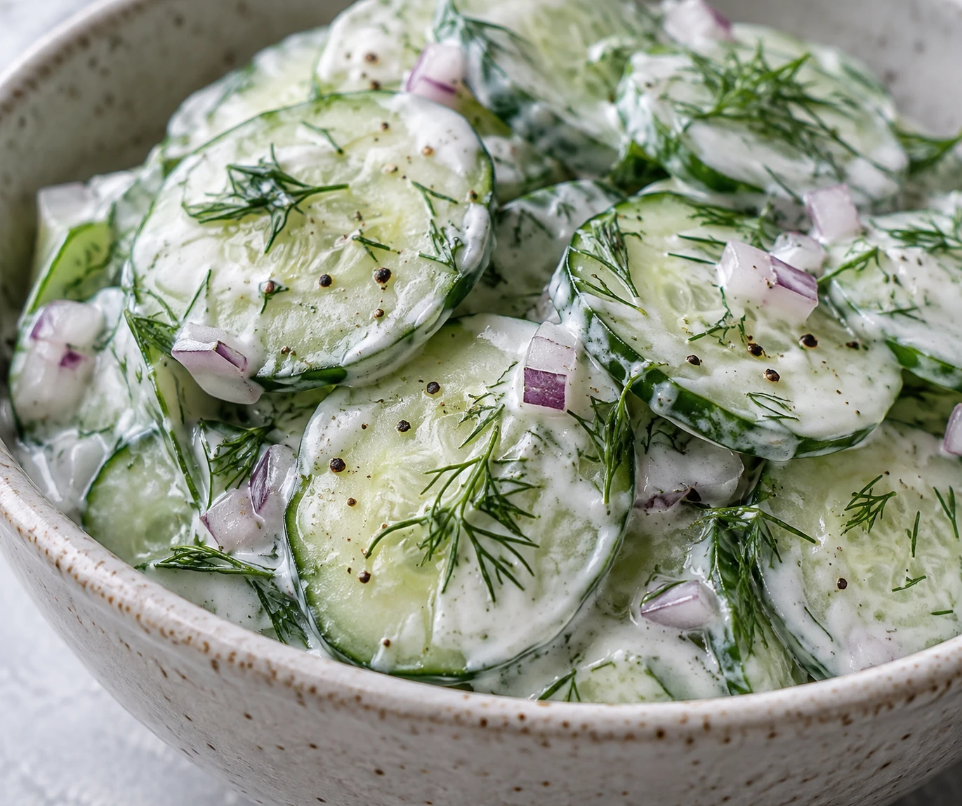 Fresh dill and black pepper speckle creamy dressing clinging to thin cucumber slices.