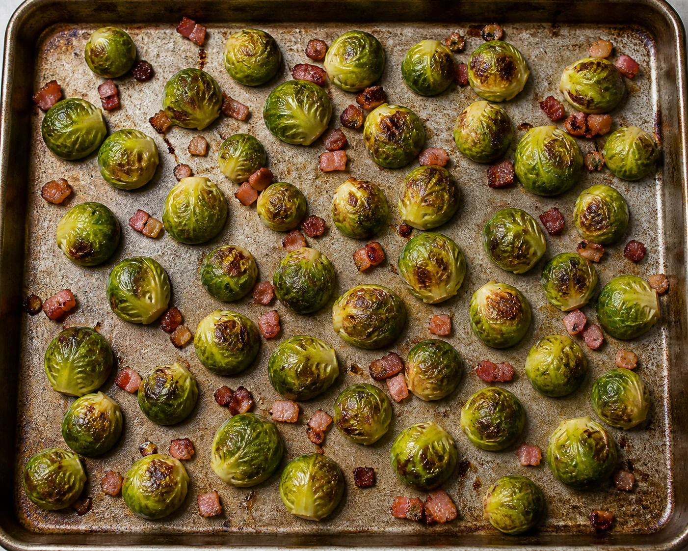 Halved Brussels sprouts sit cut side down in a single layer on a rimmed sheet pan during roasting.