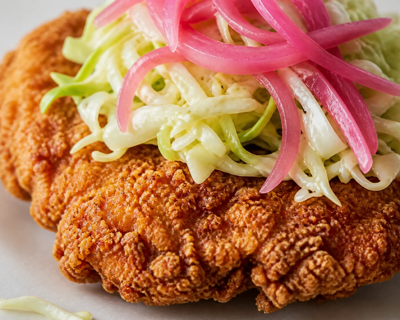 A golden craggy chicken cutlet is topped with crisp cabbage slaw and quick-pickled onion.