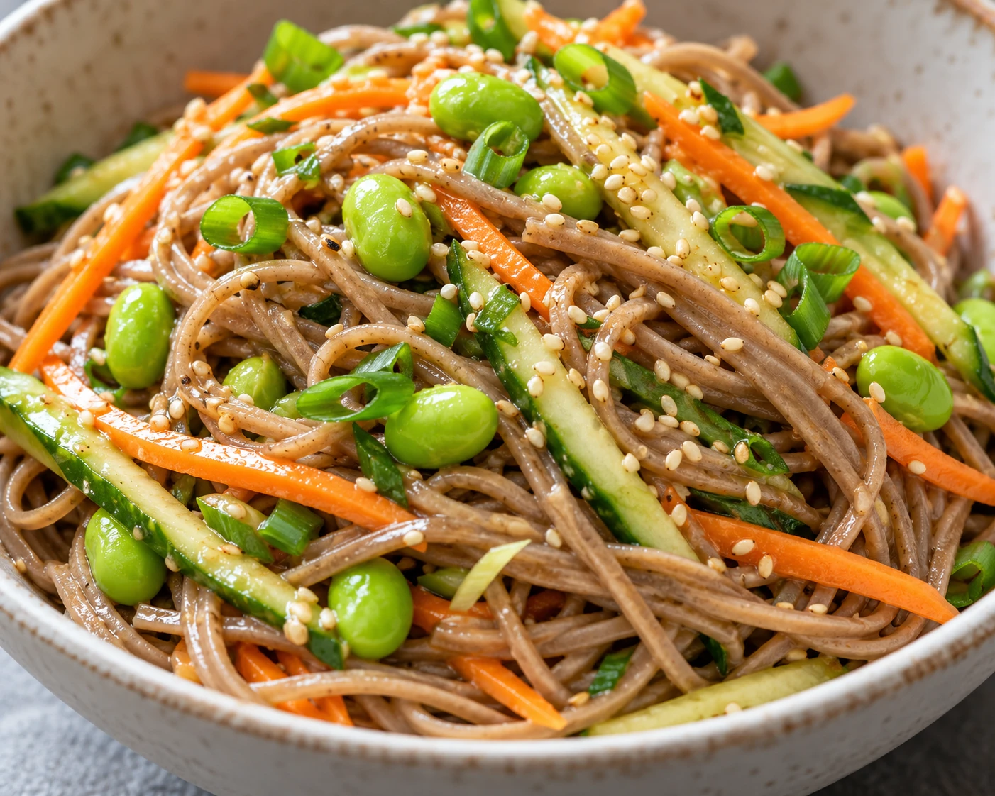 Glossy soba strands and edamame sit among crisp cucumber, carrot, scallion, and sesame seeds.