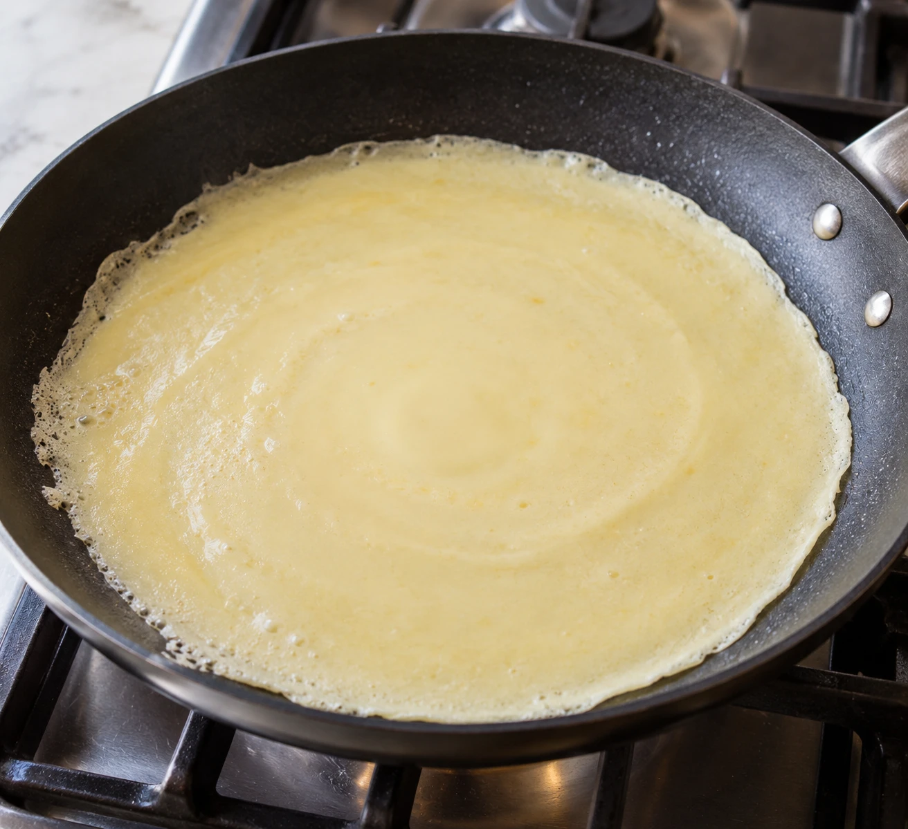 Loose crepe batter spreads into a thin layer across a lightly buttered nonstick skillet.