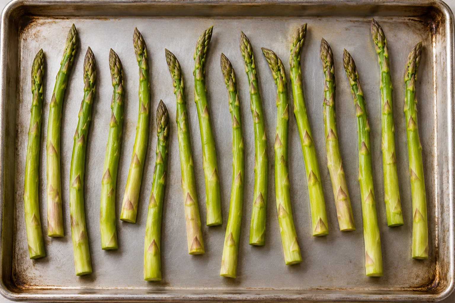 Dry asparagus spears lie in a spaced single layer on a rimmed sheet pan before roasting.