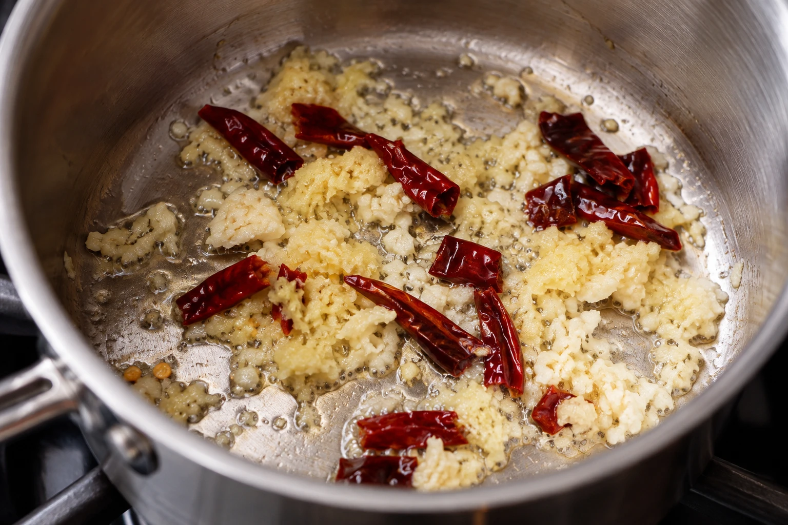 Grated garlic and ginger warm beside dried red chiles in oil in a small saucepan.