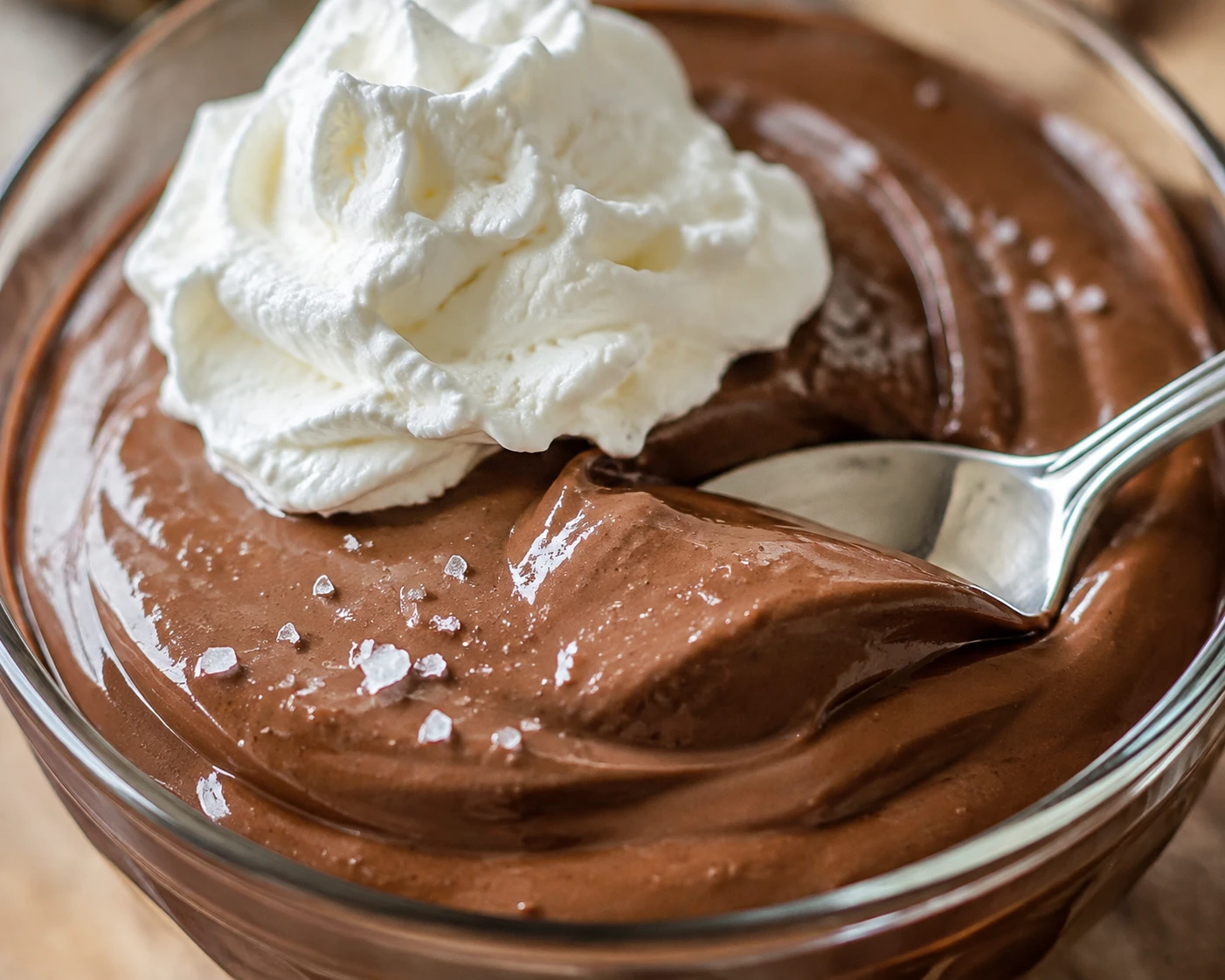 A close view of silky chocolate pudding with a soft whipped cream swirl and delicate sea salt crystals.