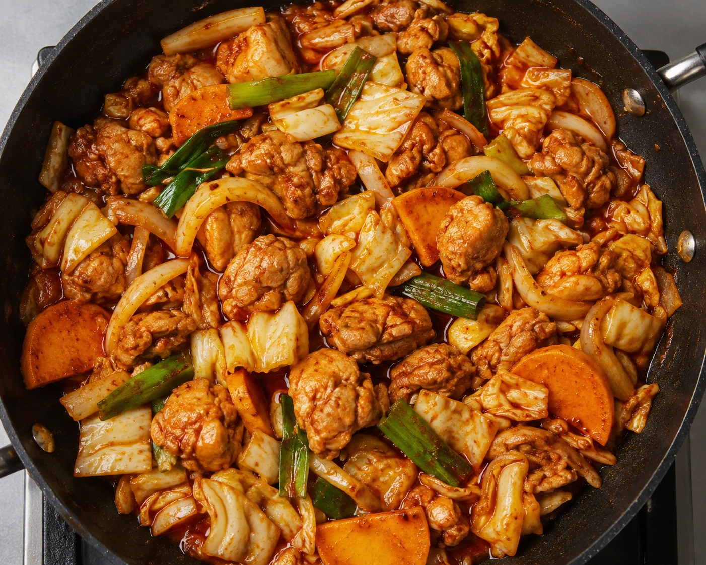 Chicken, cabbage, sweet potato, and scallions cook in red sauce in a large skillet.