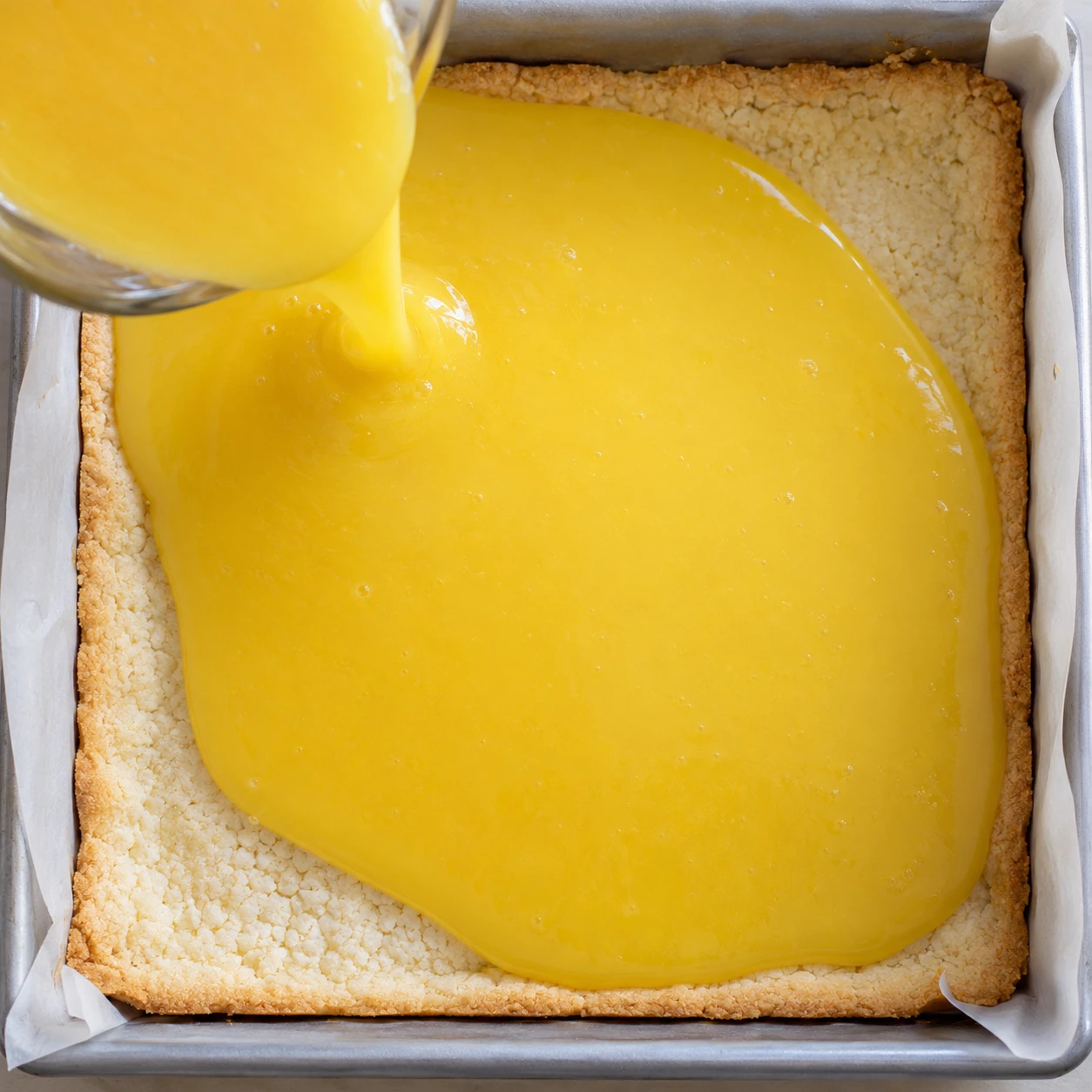 Smooth lemon filling covers the lightly golden shortbread crust in a parchment-lined square pan.