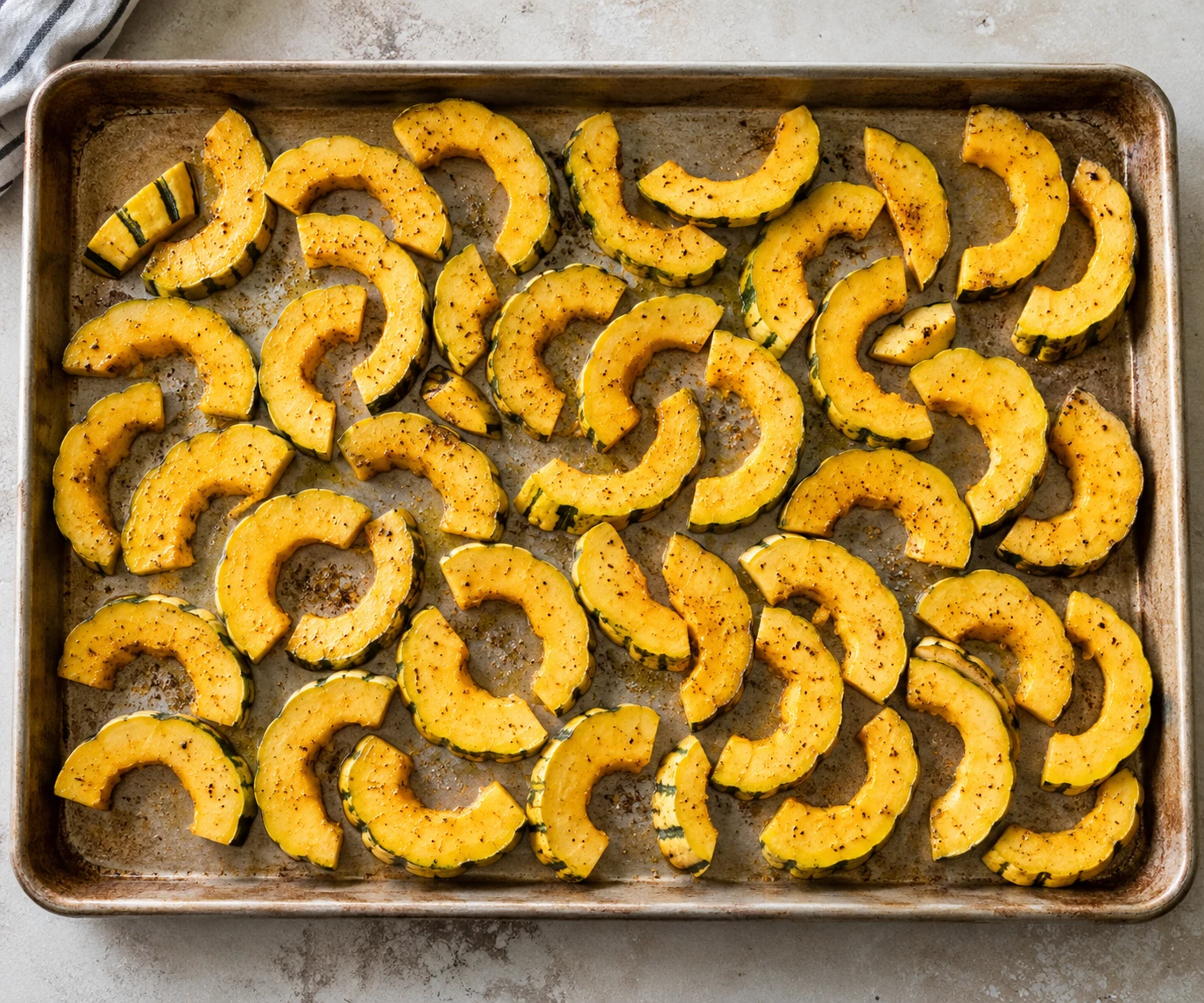 Olive-oil-seasoned delicata half-moons with pepper and thyme are spaced across a sheet pan.