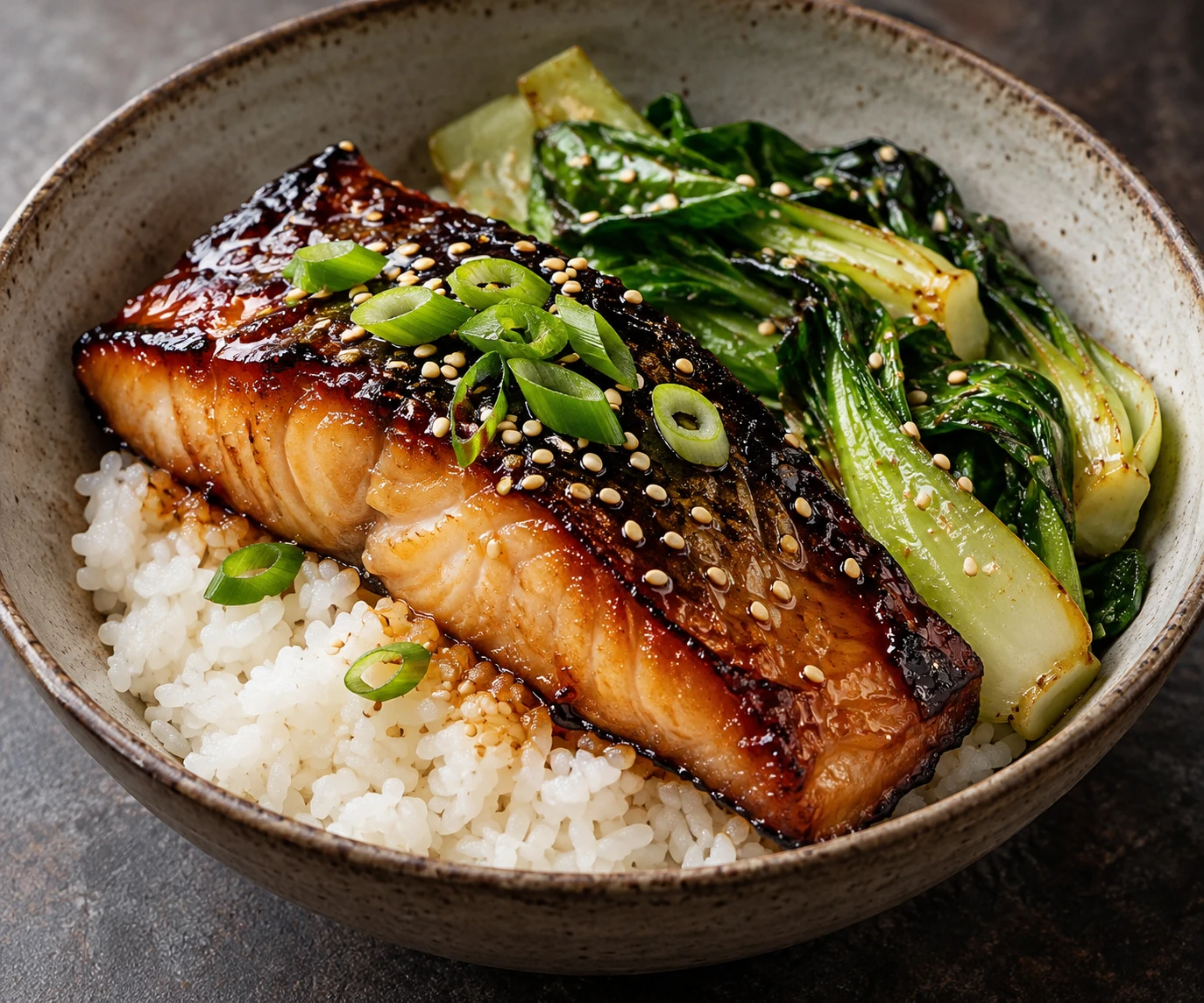 Glossy miso-glazed black cod sits with sesame bok choy and rice in a ceramic bowl.