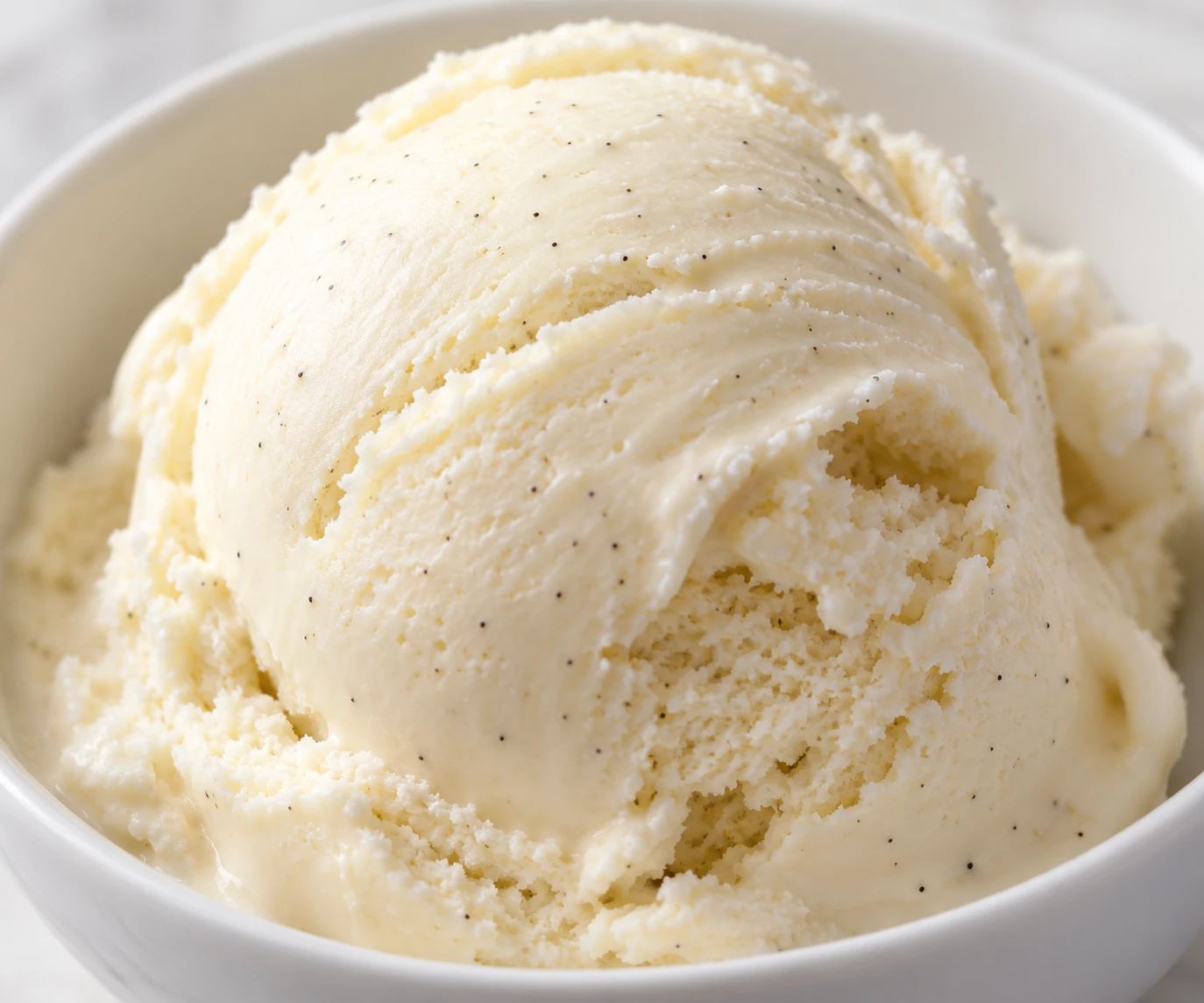 A close creamy curl of vanilla ice cream reveals fine vanilla bean flecks and a smooth texture.