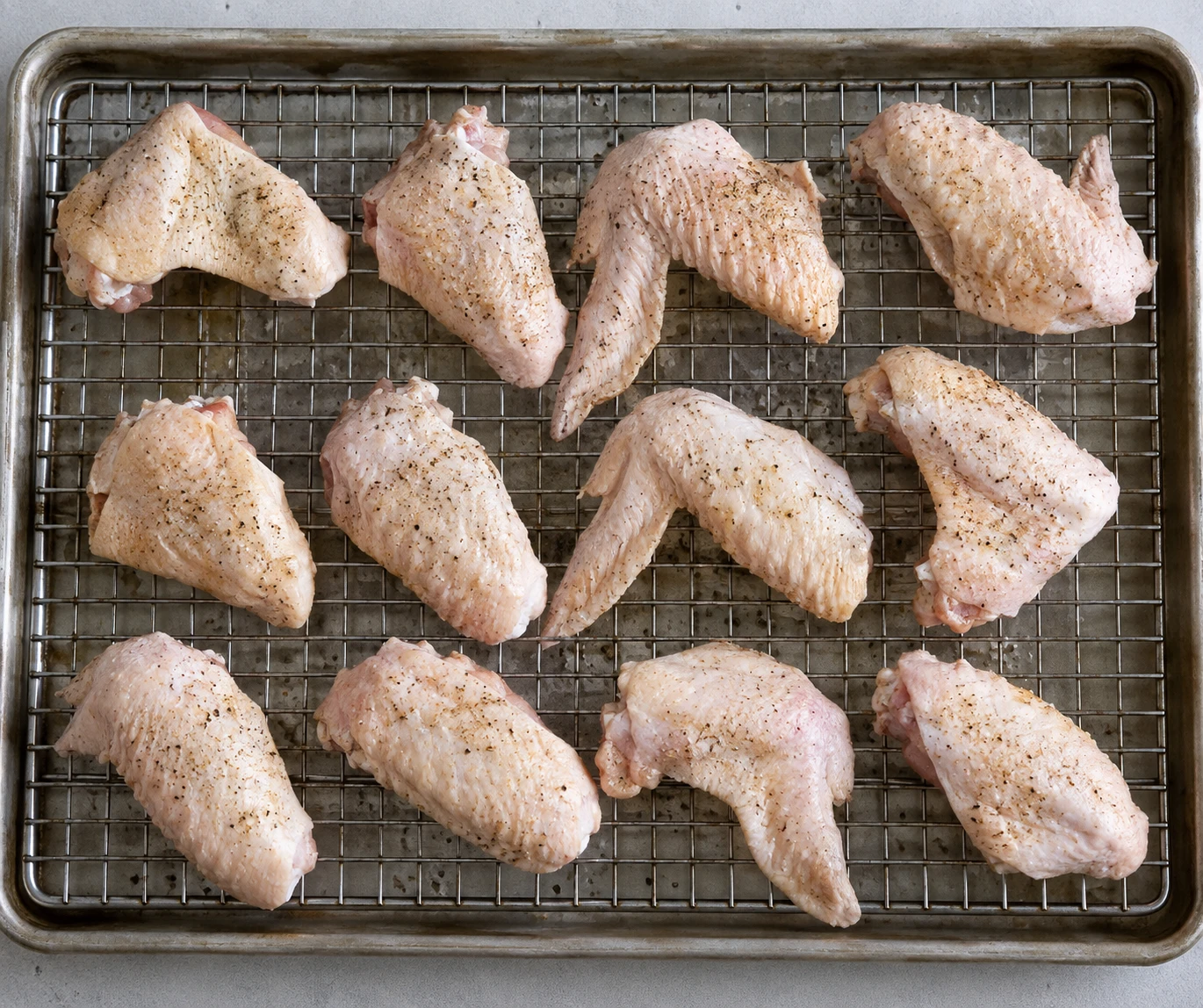 Dried and seasoned chicken wings are spaced skin-side up on a wire rack over a rimmed pan.