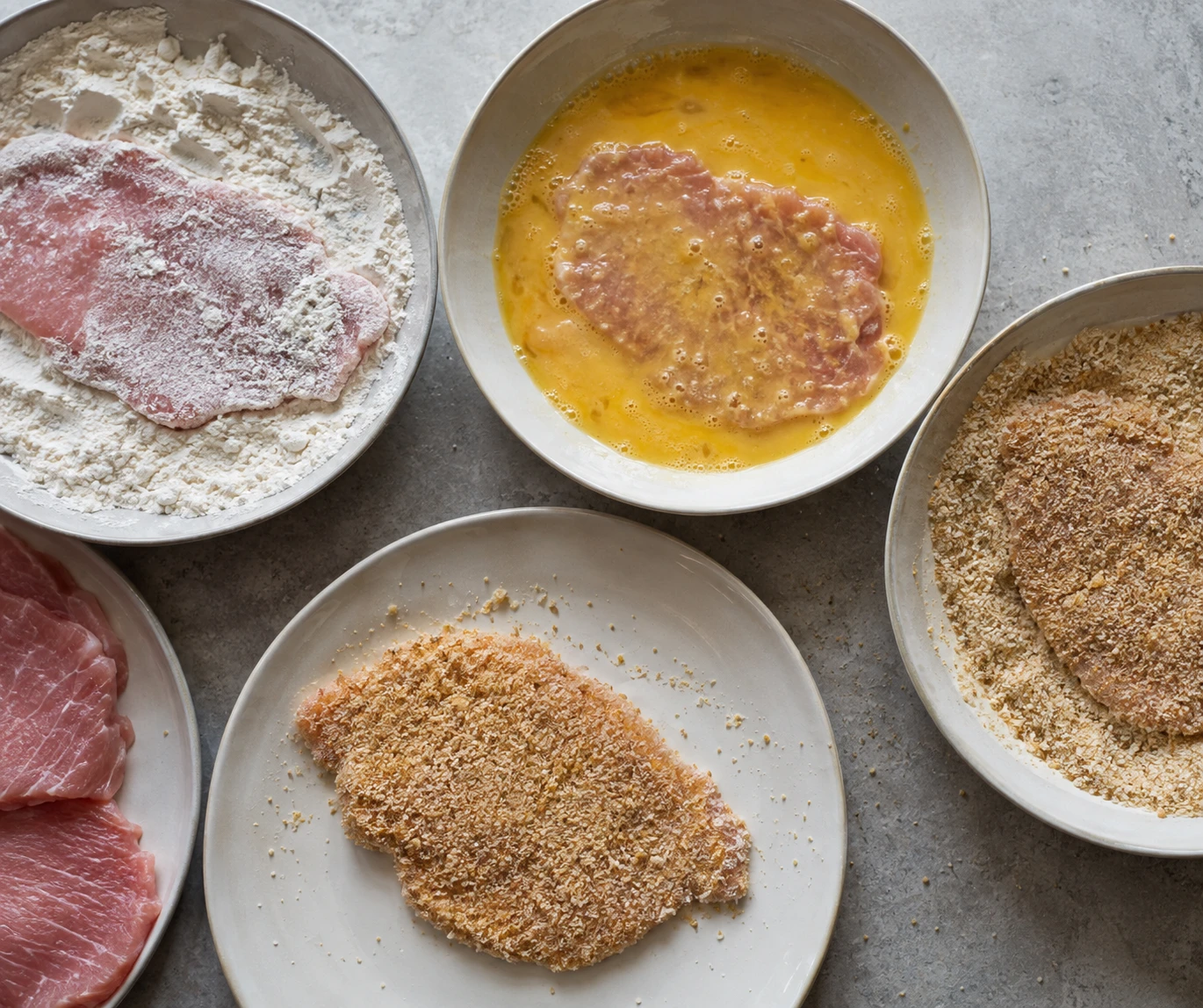 Thin pork cutlets move through flour, beaten egg, and breadcrumbs before shallow frying.