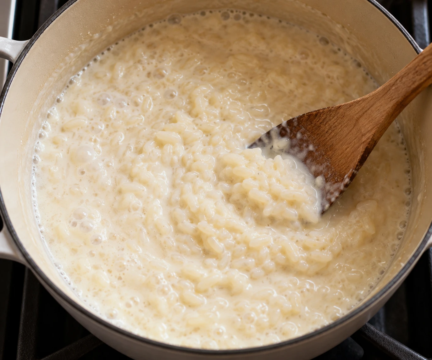 Rice simmers in milk in a saucepan while a wooden spoon moves through the thickening mixture.