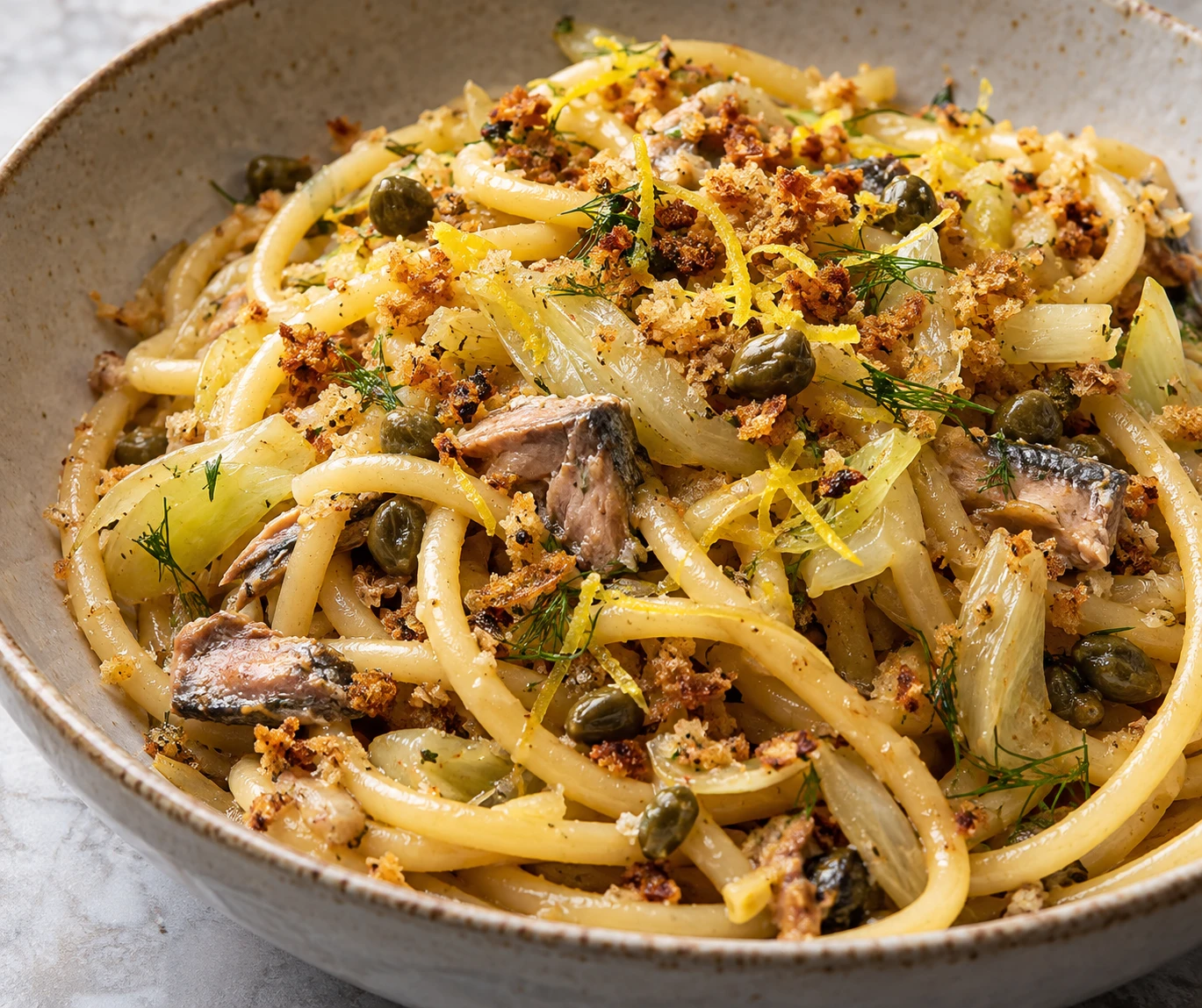 Glossy bucatini holds visible sardine flakes and fennel beneath crisp golden crumbs.