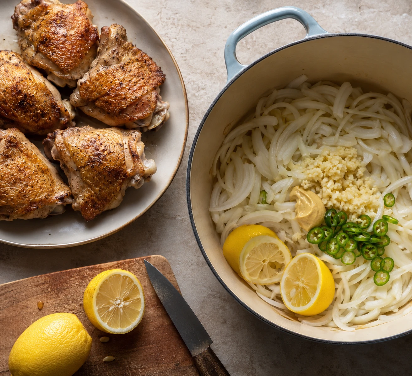 Browned chicken thighs sit beside a Dutch oven of sliced onions, lemon, mustard, garlic, and chile for yassa.