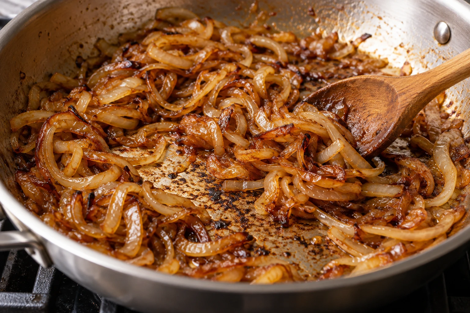Deep amber onions and loosened brown fond fill a wide stainless-steel skillet during slow caramelization.