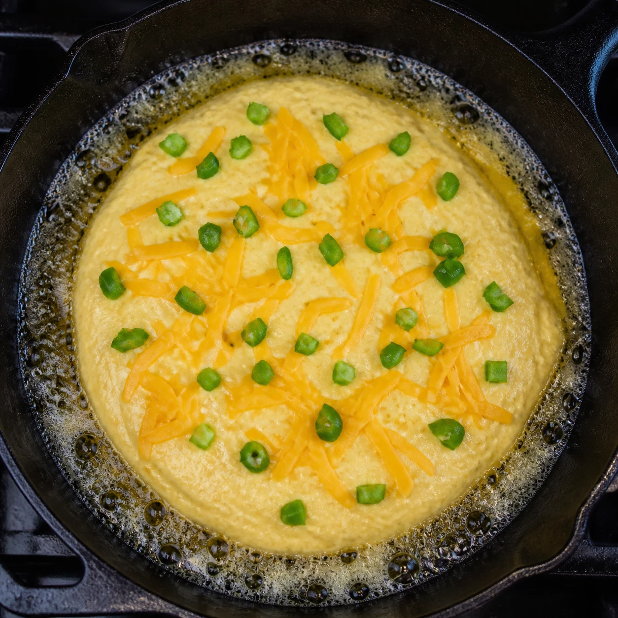 Cornbread batter in a buttered cast-iron skillet topped with sharp cheddar and diced jalapeño before baking.