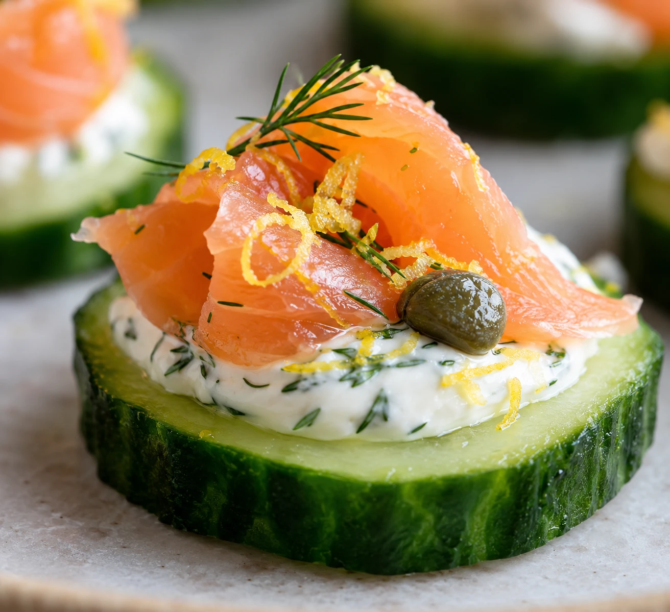 A single cucumber bite shows its crisp edge, dill cream, smoked salmon, caper, and fine lemon zest.