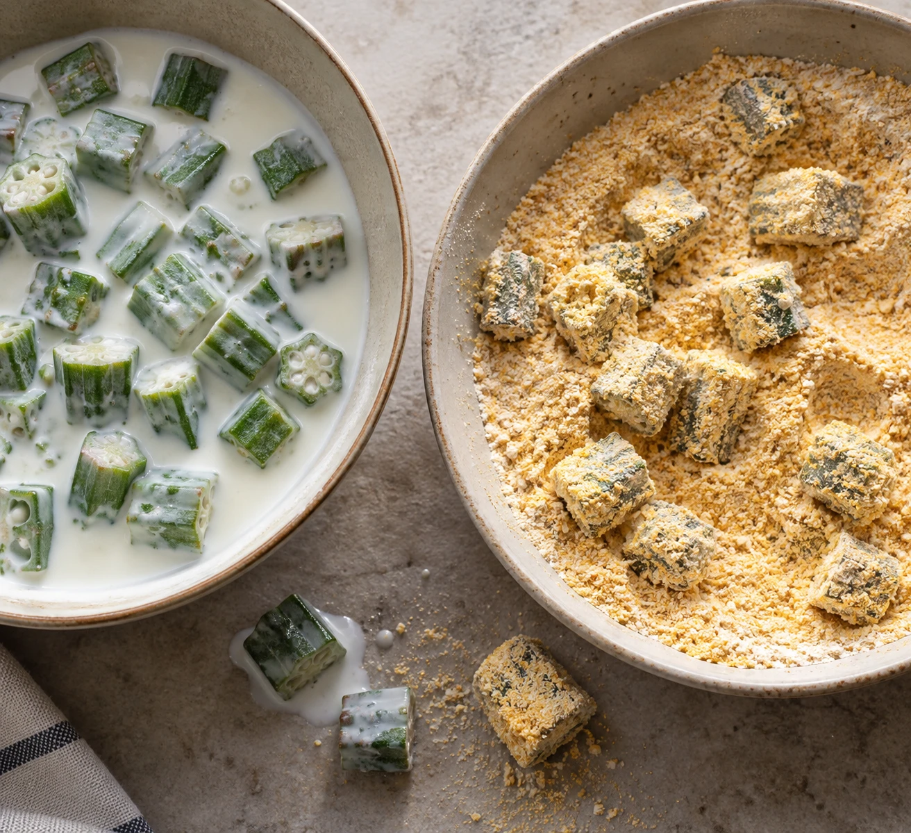 Fresh okra pieces receive a thin buttermilk dip beside a bowl of seasoned cornmeal coating.