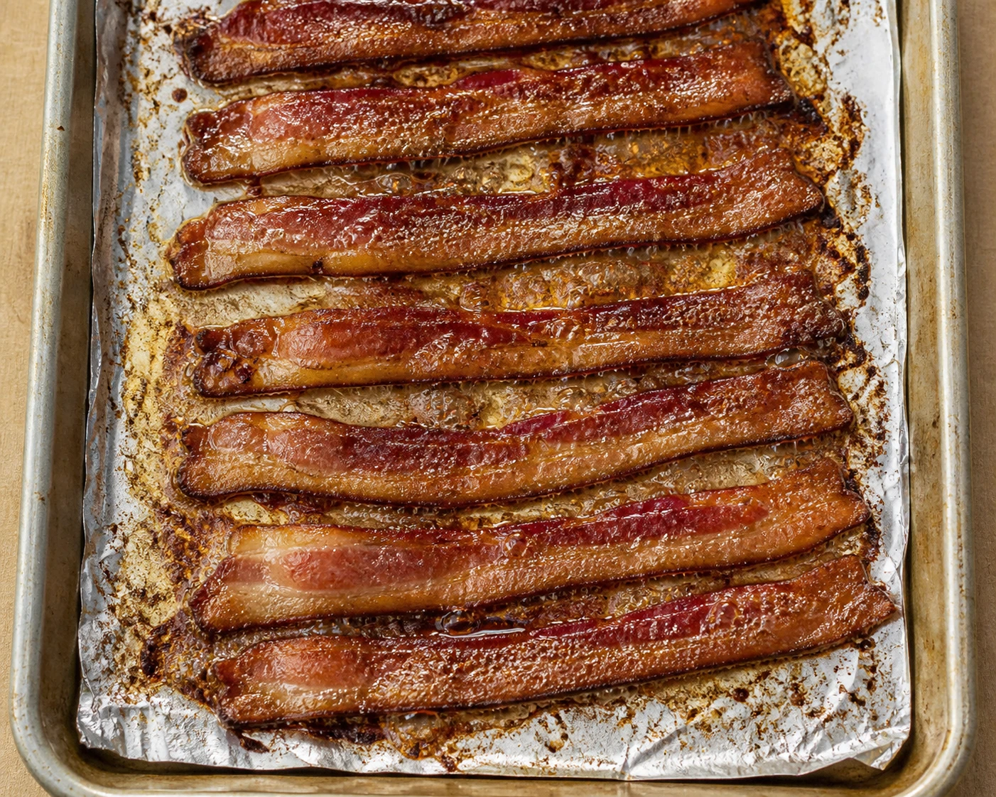 Deeply browned thick-cut bacon crisps in a single layer on a foil-lined sheet pan.