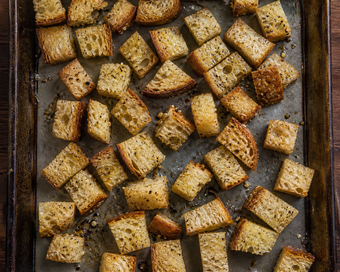 Garlic and black-pepper seasoned sourdough cubes bake on a sheet pan to become Caesar croutons.