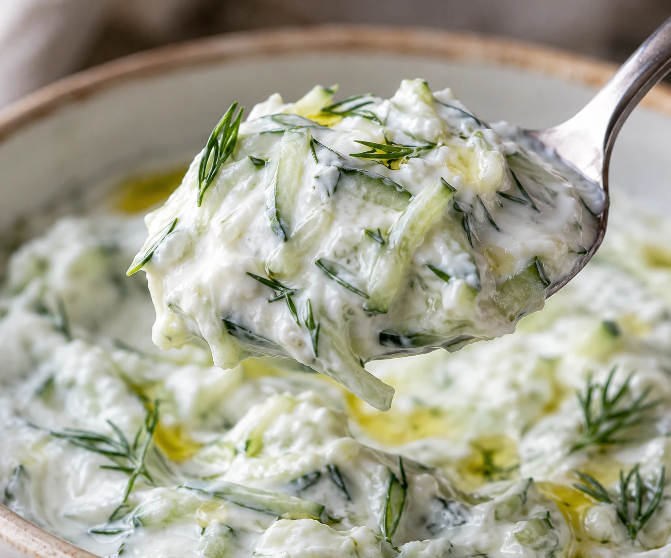 A spoon lifts thick tzatziki with cucumber shreds, dill, and a subtle olive-oil gloss.