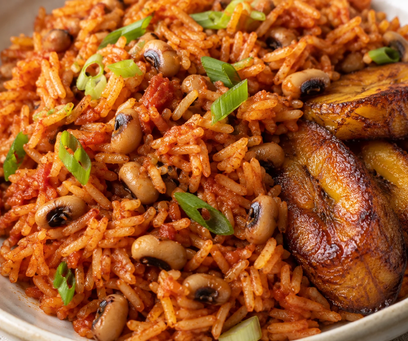 Separate tomato-red rice grains, intact black-eyed peas, scallions, and a caramelized plantain edge.