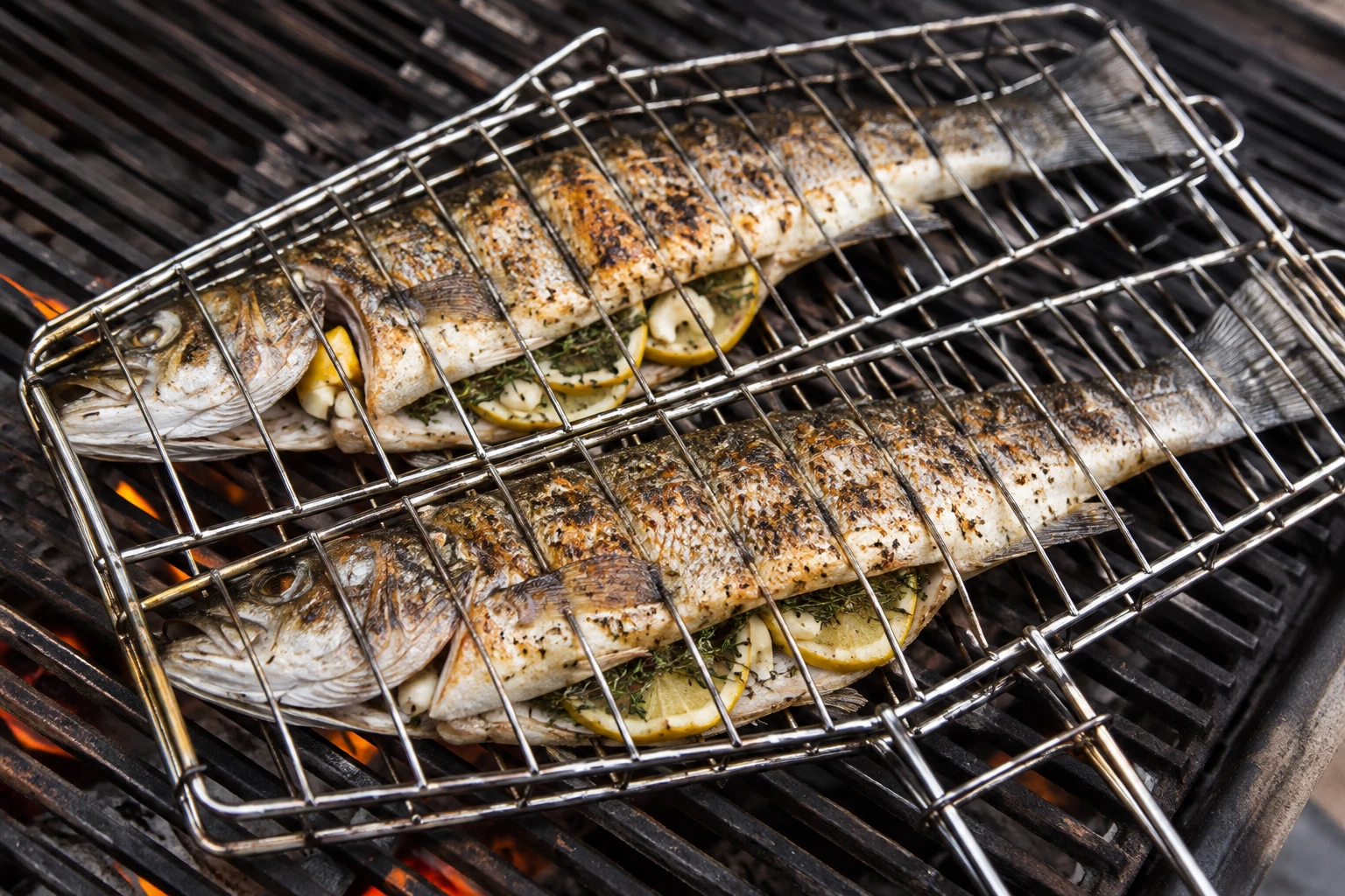 Lemon- and oregano-stuffed branzini grill inside a hinged basket over the grate.